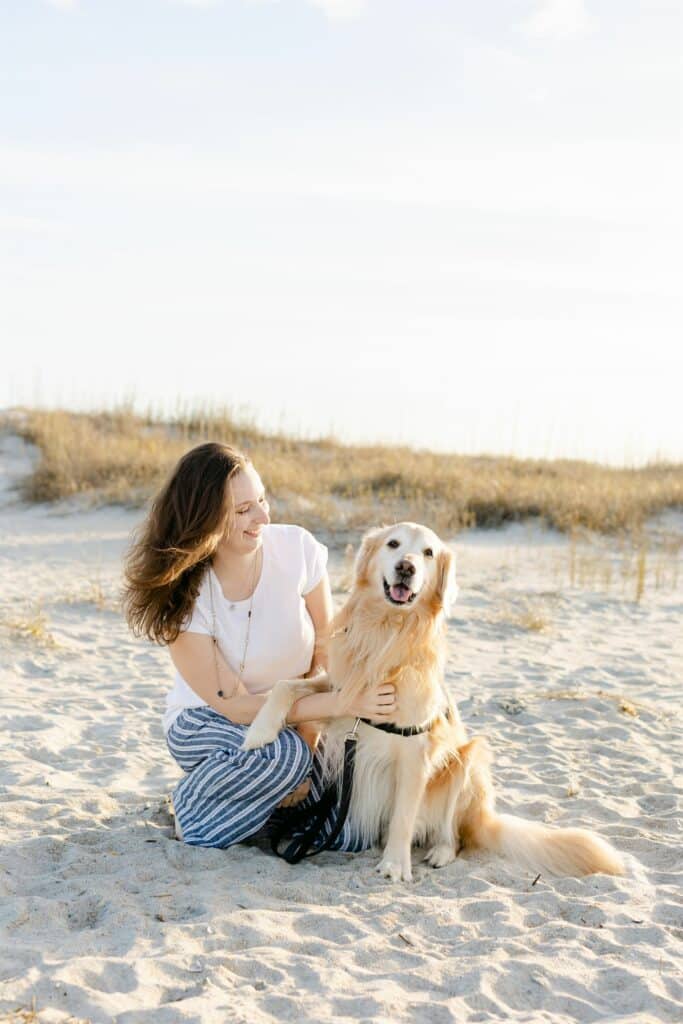 golden retriever service dog sitting on beach with handler kneeling next to it