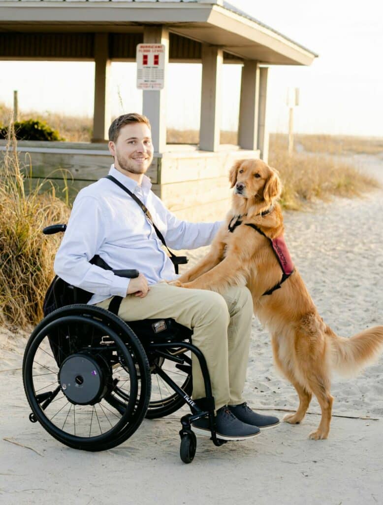 Assistance Dog Program Member with Golden Retriever in vest standing with front paws on handler in wheelchair