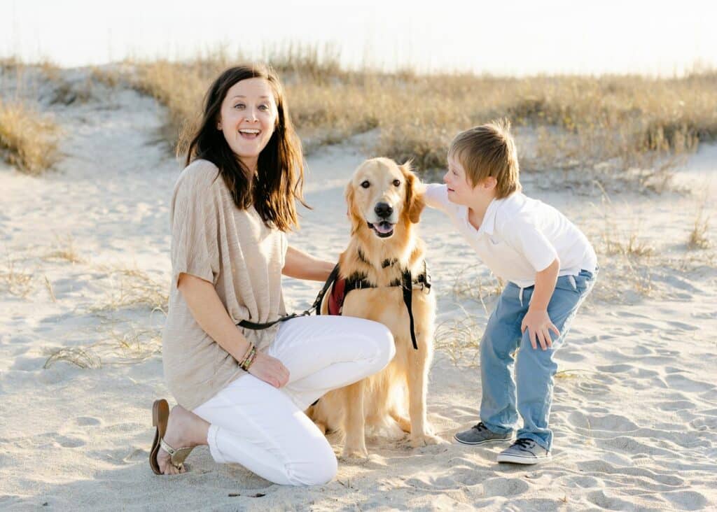 woman and child smiling with golden retriever dog in service vest