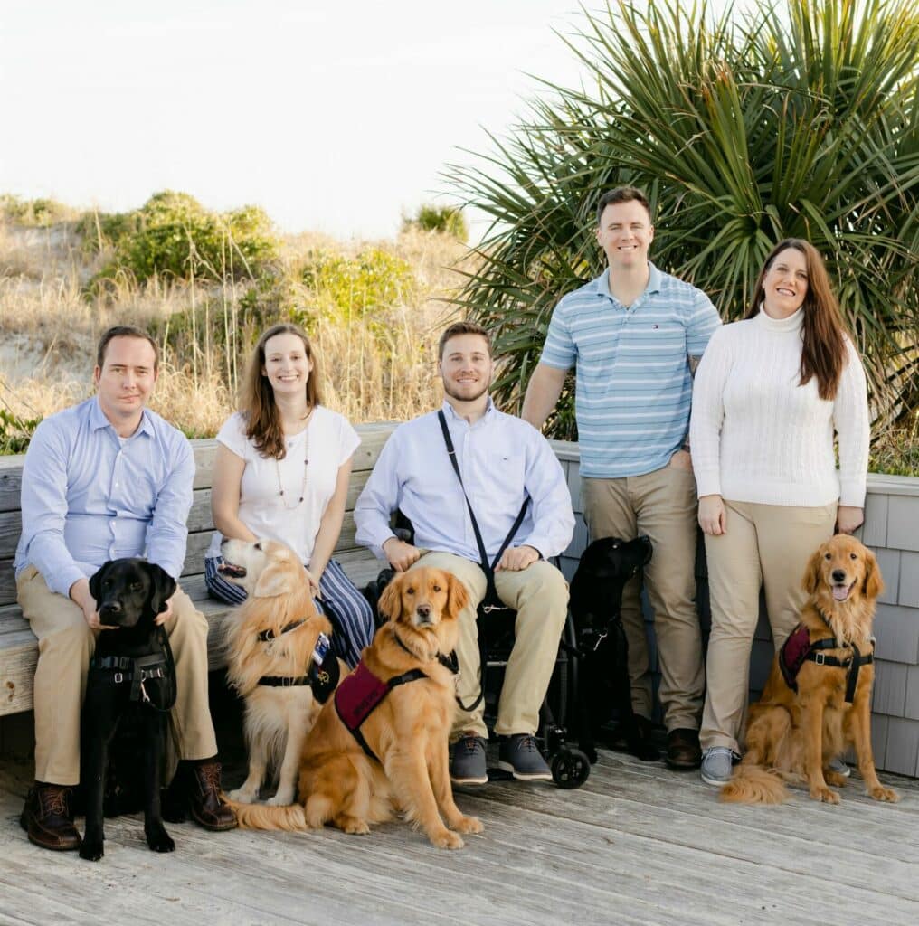 group of five service dogs in training vests sitting with their handlers