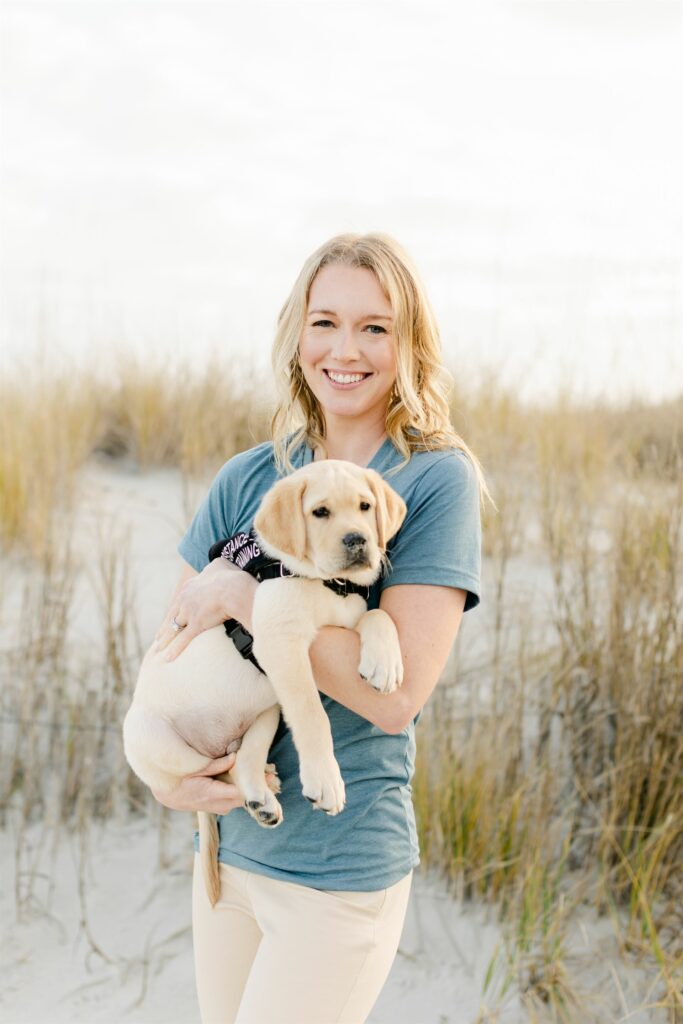 paws4people team member Kaitlin Bellamy holding yellow lab puppy in assistance dog in training vest